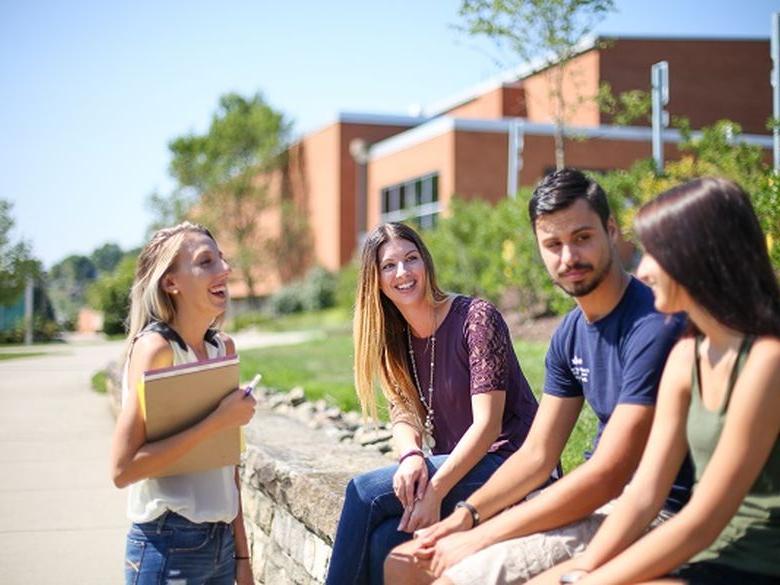 students on campus sitting on the wall outside Athletics building