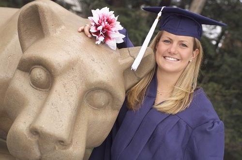 graduating female student standing at lion shrine in cap and gown leaning on lion
