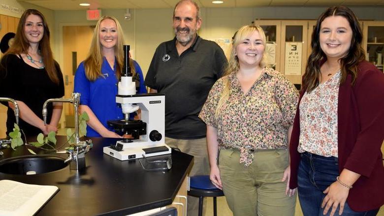五个人站在一张放着显微镜的实验台上