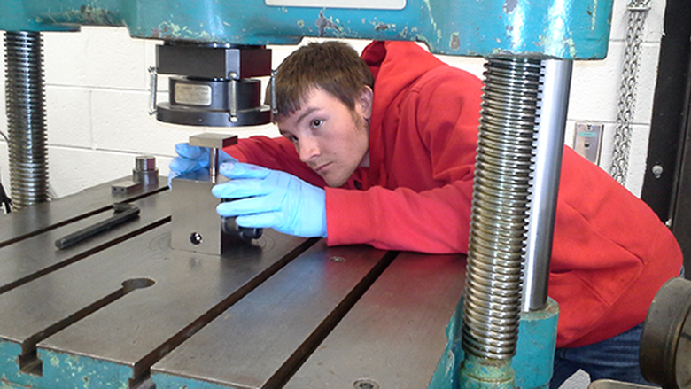 Person in a red hoodie and blue gloves works with a metal machine
