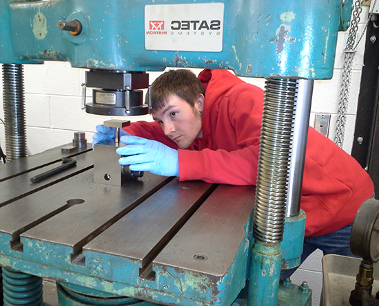 Person in a red hoodie and blue gloves works with a metal machine
